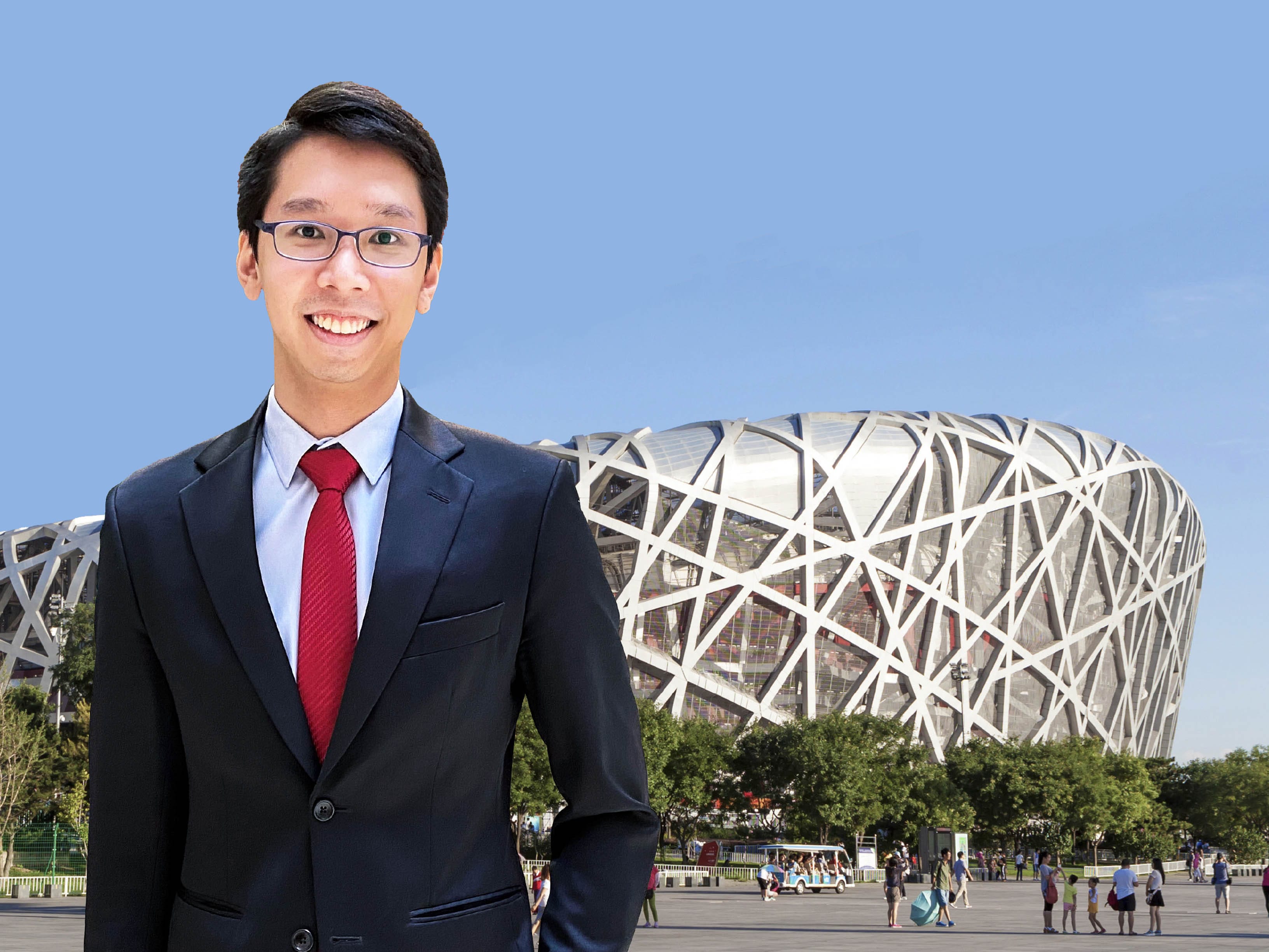 A man in a formal suit, smiling, stands in front of the Bird’s Nest Stadium in Beijing.